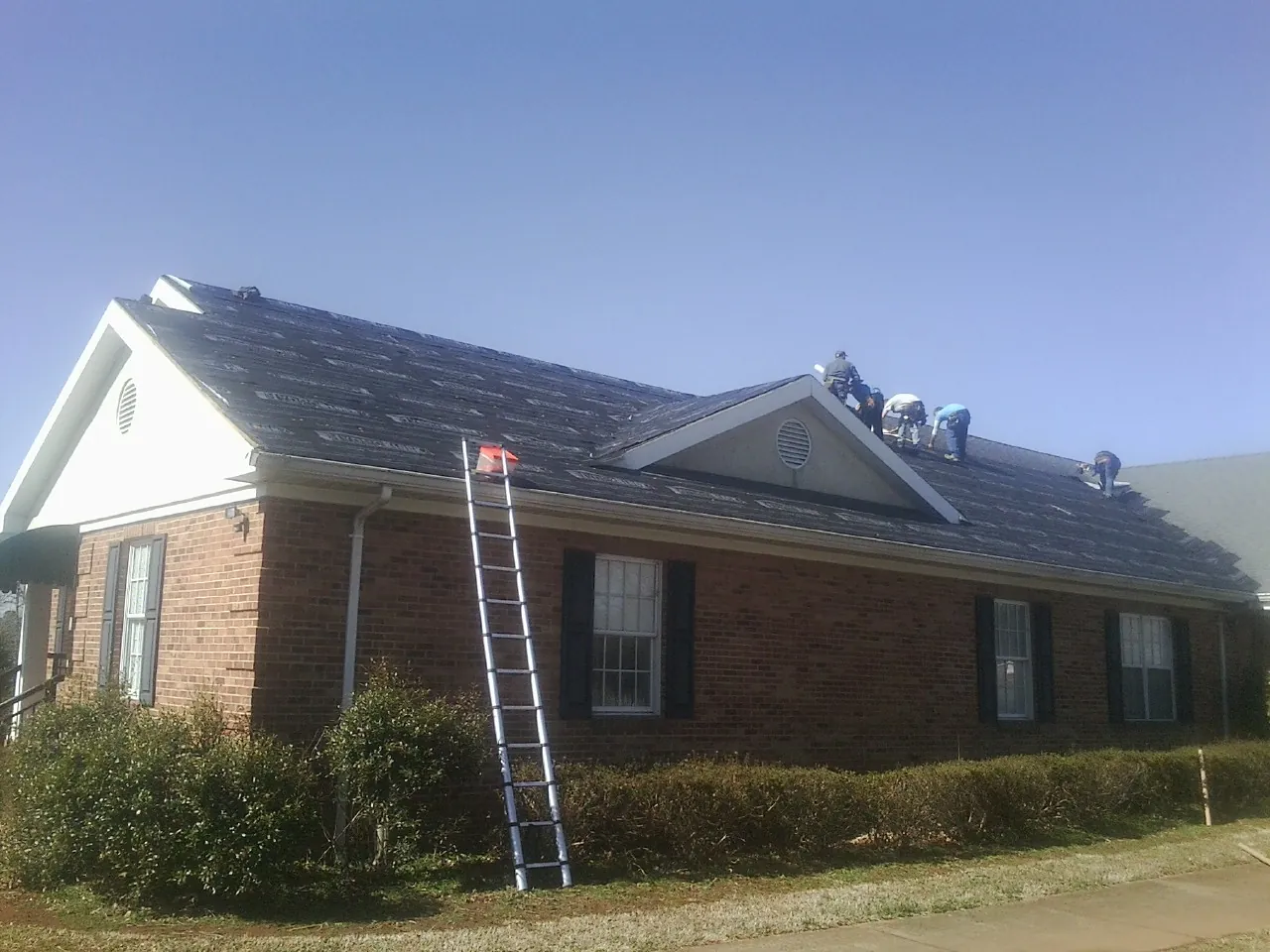 Crew tearing shingles off a brick ranch roof with a ladder set — Metal Roof Repair work by our crew in Wauregan
