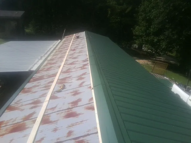 Old rusted panels beside newly installed green metal roofing — Wind Damage Roof Repair by Roofing Brothers in Wauregan