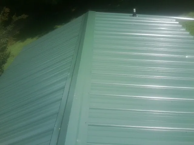 New green metal panels meeting at the ridge of a roof — Flat Roof Repair work by our crew in Wauregan