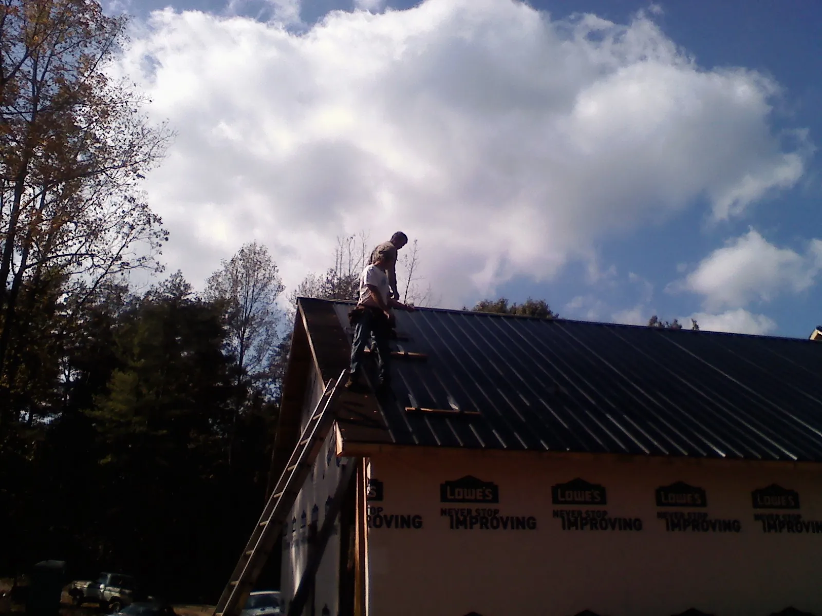 Roofer fastening dark metal panels high against a cloudy sky, from a Roof Inspection job in Wauregan
