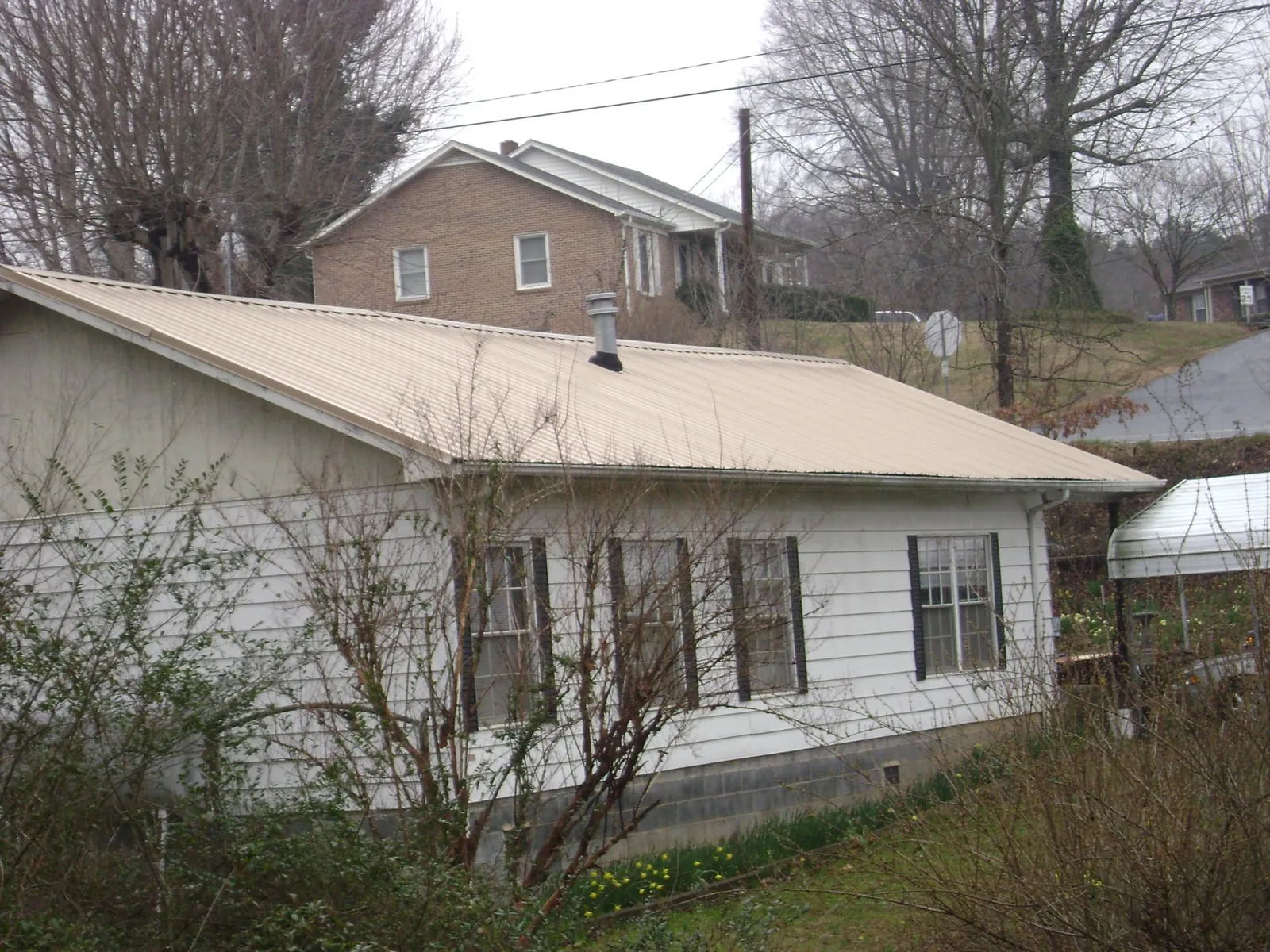 Tan metal roof on a white sided house set into a hillside — Commercial Roofing by Roofing Brothers in Wauregan